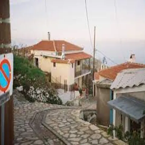 Σοκάκι με πέτρινα σπίτια στους Κοσμαδαίους Σάμου με φόντο τη θάλασσα.